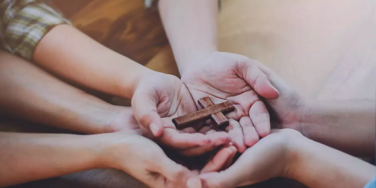 Three people hands holding small wooden cross on wood table, Chr